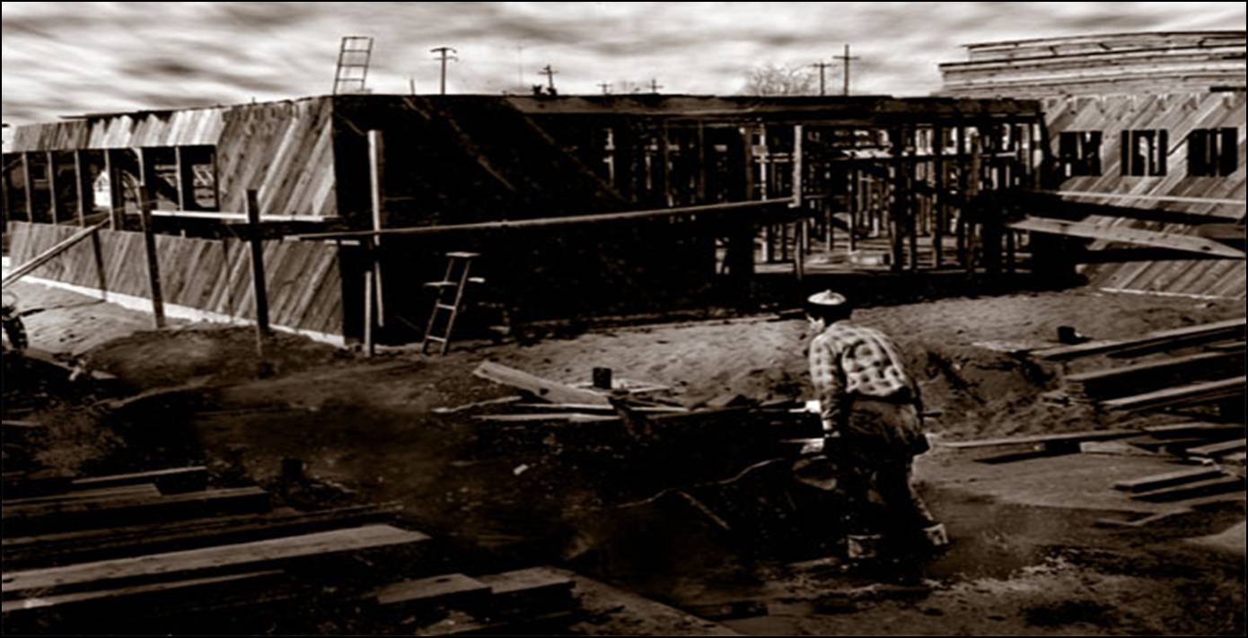 Historic 1955 black and white photograph of construction progress showing the exterior walls and roof enclosure of the 200-seat parish hall facility nearing completion. A construction worker is in foreground.