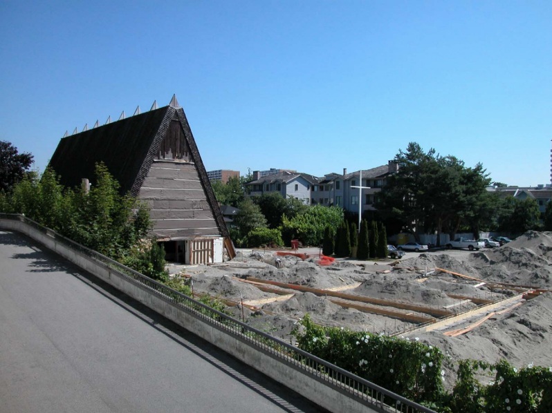 A photograph showing site preloading, foundation work, and rebar for the new multi-use facility at Trinity Lutheran Church in Richmond, BC. The south elevation of the existing A-frame church building is visible.