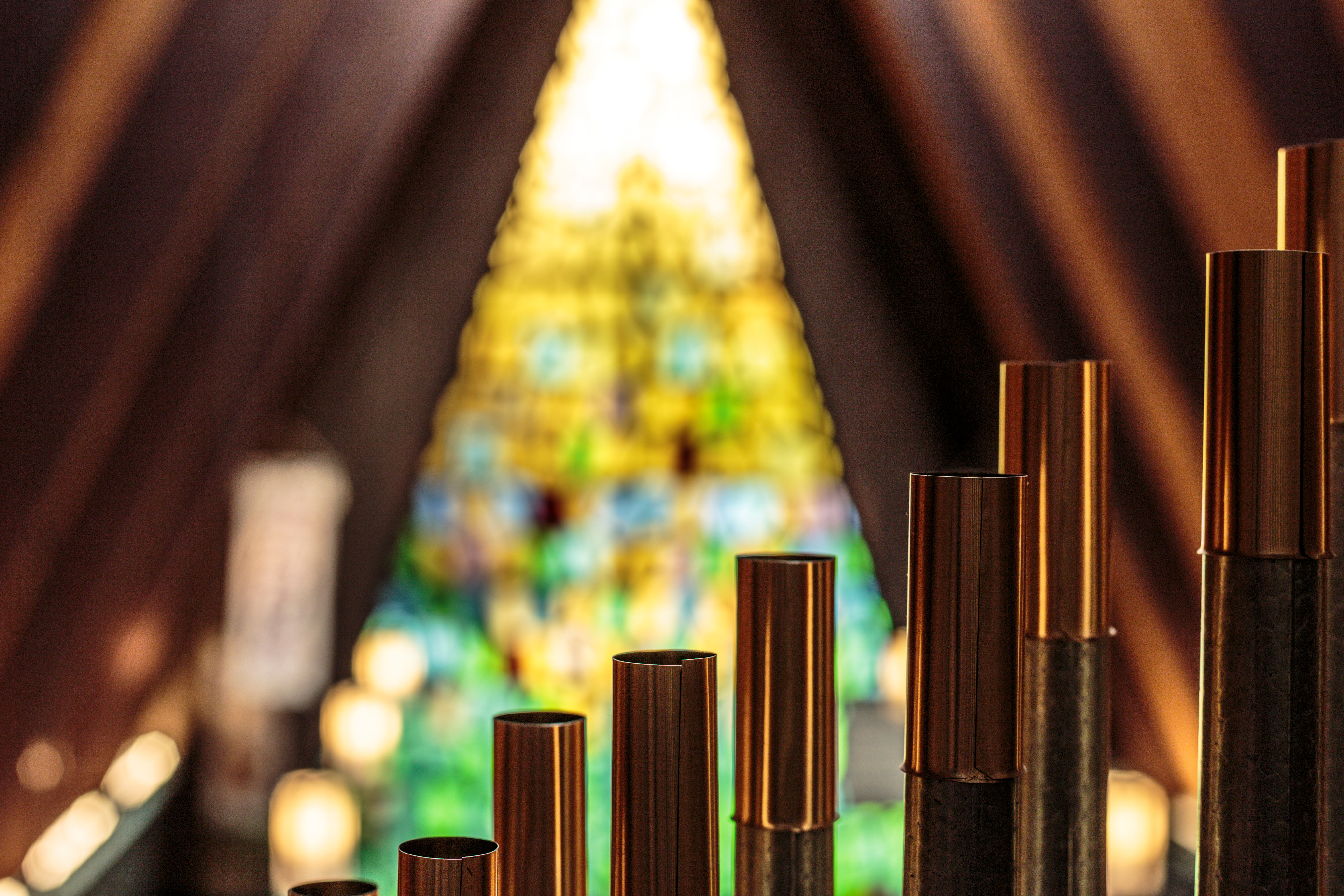 Close-up of copper-topped Wicks organ pipes at Trinity Lutheran Church, Richmond with A-frame sanctuary and triangular floor-to-ceiling stained-glass window in background. Photo by A. Schwab